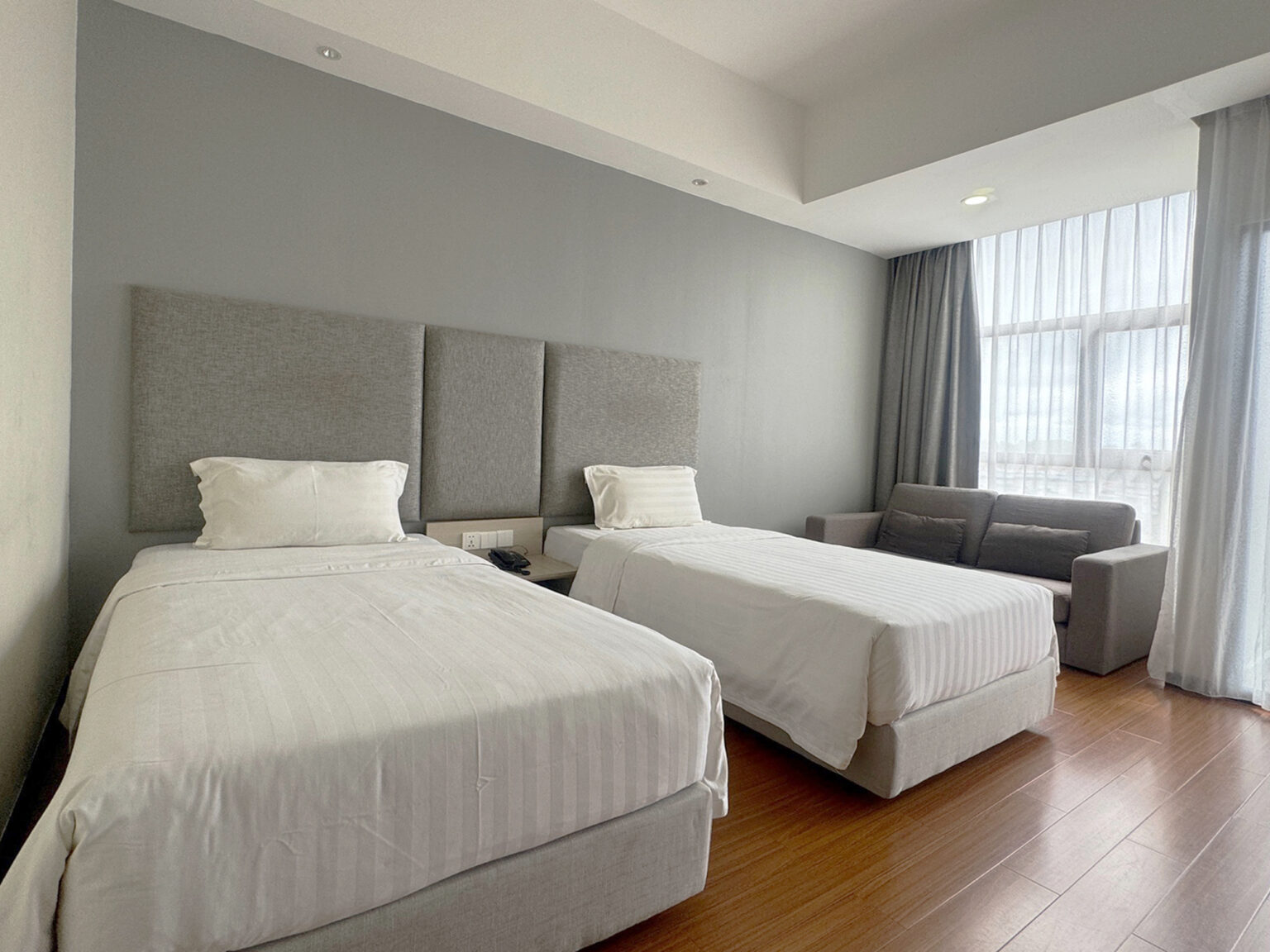Interior of Deluxe Twin Room at Livingston Hotel Sandakan showing twin beds, sofa, telephone, curtains, and balcony