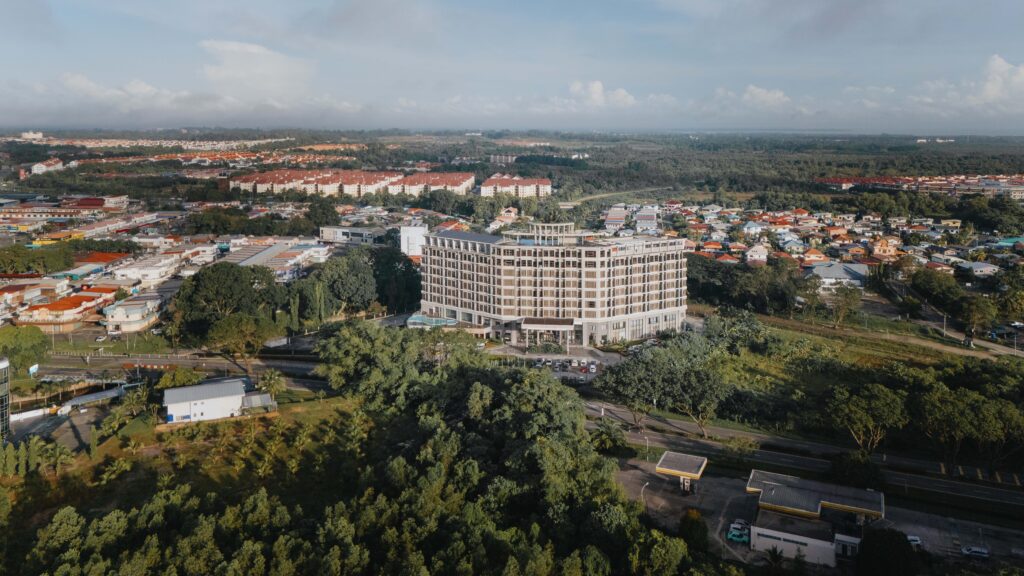 Drone view of Livingston Hotel Sandakan showing nearby petrol station, streets, outdoor swimming pool, and drop-off area