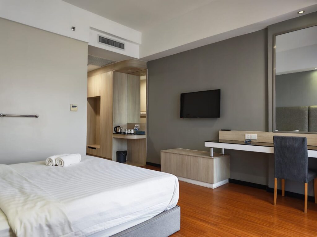 Accessible room with bed, TV, wardrobe with lowered hanging rail, chair, and bedside grab bar at Livingston Hotel Sandakan Sabah