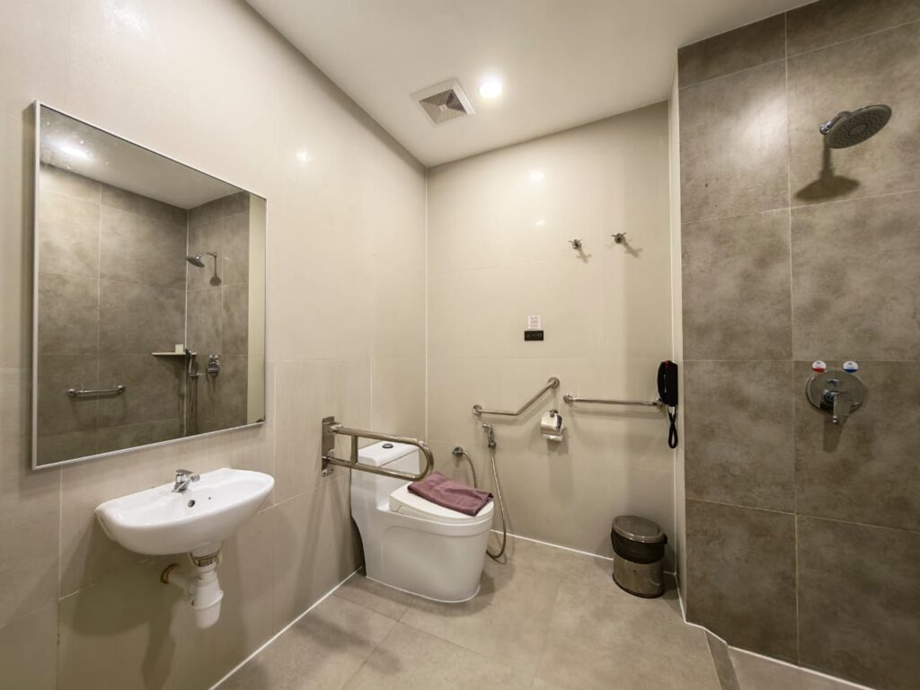 Accessible bathroom with grab bars, wheelchair-friendly layout, toilet, sink, and mirror at Livingston Hotel Sandakan Sabah